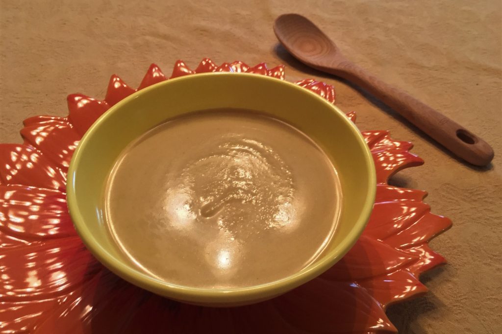 yellow bowl of curried cauliflower soup on flower-shaped charger with wooden spoon