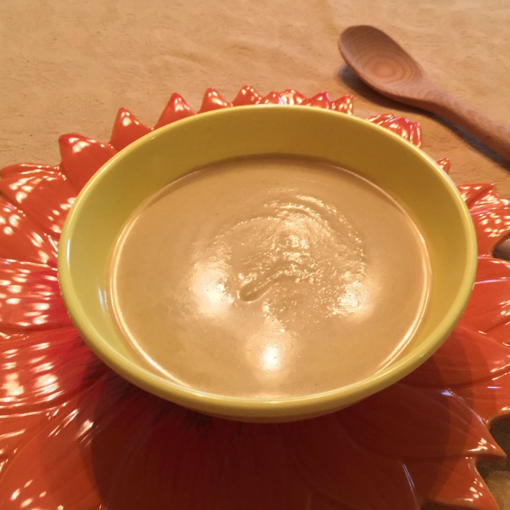 yellow bowl of curried cauliflower soup on an orange flower-shaped charger with a wooden spoon