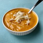 bowl of pumpkin chickpea soup and shredded cheese with a spoon