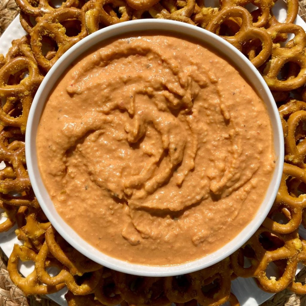 bowl of homemade roasted red pepper hummus surrounded by garlic herb pretzels