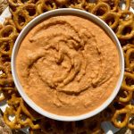 bowl of homemade roasted red pepper hummus surrounded by garlic herb pretzels