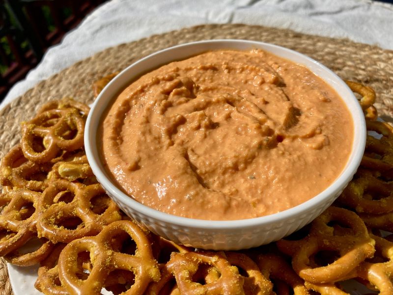 bowl of homemade roasted red pepper hummus surrounded by garlic herb pretzels