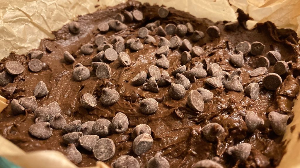 double chocolate sweet potato brownie batter topped with chocolate chips in a parchment-lined baking dish